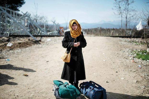 TOPSHOT - A young migrant woman from Syria stands with her bags after crossing the Greek-Macedonian border near the town of Gevgelija on February 23, 2016. Greece has expressed "displeasure" to the EU over tougher border controls by Balkan countries that have stranded thousands of migrants in the country, Prime Minister Alexis Tsipras' office said on February 23. / AFP / Robert ATANASOVSKI